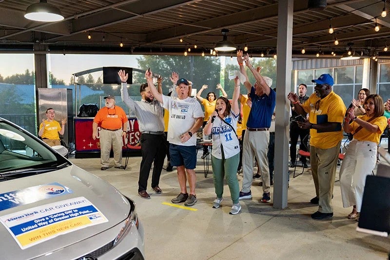 Group of people cheering and celebrating at a community event near car