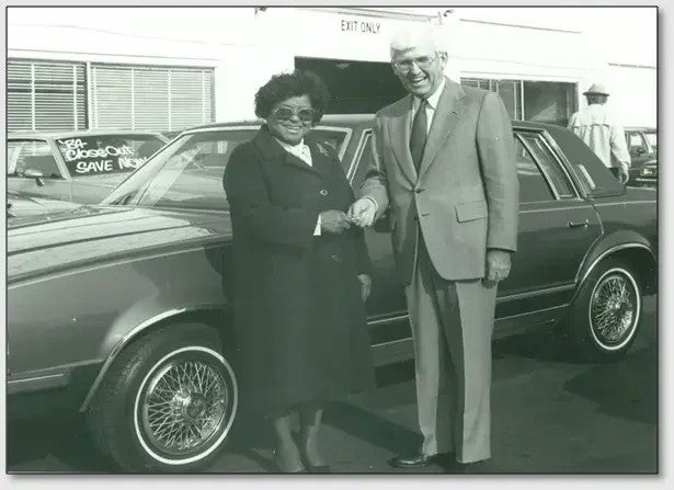 Historic black-and-white photo of two people standing beside a car