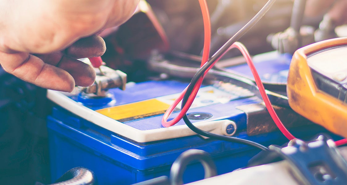 Close-up car battery being serviced, with cables and diagnostic tools connected